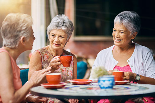 Three senior ladies having coffee and tea outside, living their best life at their independent living community. 